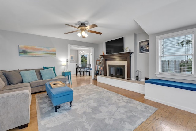 living room with a glass covered fireplace, baseboards, ceiling fan with notable chandelier, and wood finished floors