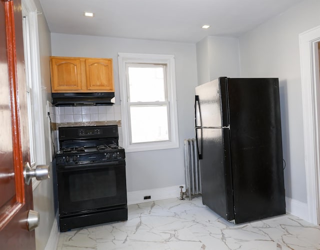 kitchen featuring decorative backsplash, under cabinet range hood, radiator heating unit, black appliances, and baseboards