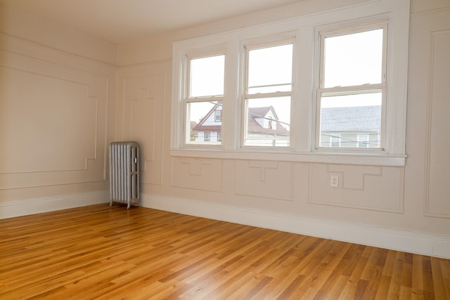 empty room featuring baseboards, radiator, light wood finished floors, and a decorative wall