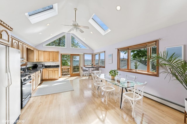 kitchen featuring a skylight, freestanding refrigerator, stainless steel gas stove, dark countertops, and baseboard heating