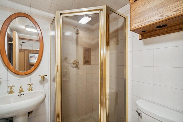 bathroom featuring a sink, a shower stall, toilet, and tile walls