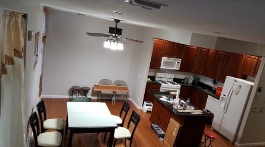 kitchen featuring ceiling fan, a kitchen island, dark countertops, wood finished floors, and white appliances