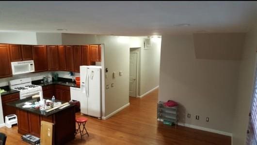 kitchen with dark countertops, white appliances, a breakfast bar area, light wood-style flooring, and a kitchen island