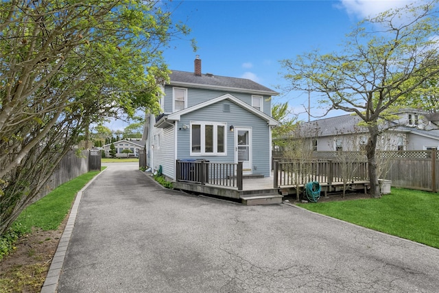 rear view of property featuring fence, a wooden deck, a chimney, and driveway