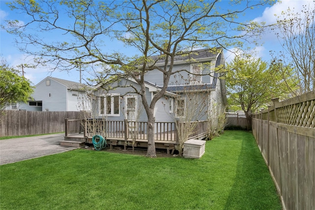 rear view of property with a lawn, a wooden deck, and a fenced backyard