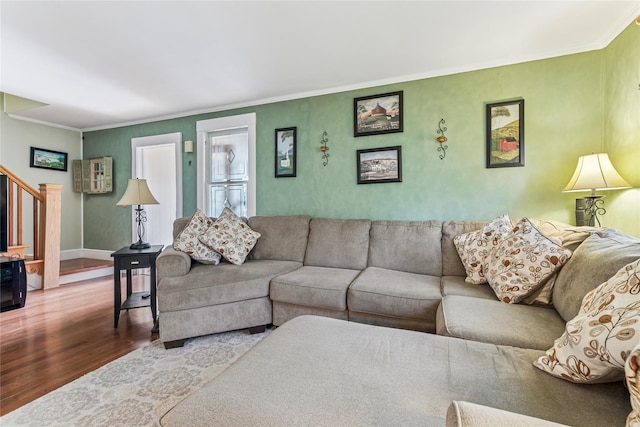 living room featuring crown molding, baseboards, wood finished floors, and stairway
