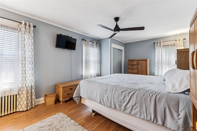 bedroom with ceiling fan, crown molding, wood finished floors, baseboards, and a closet