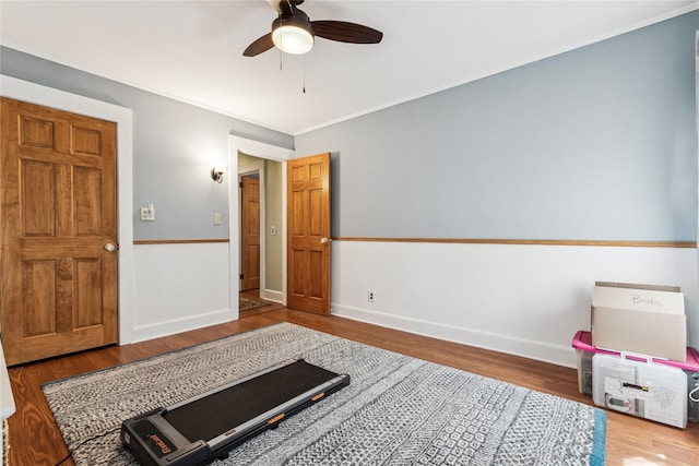 exercise room featuring baseboards, ceiling fan, ornamental molding, and wood finished floors
