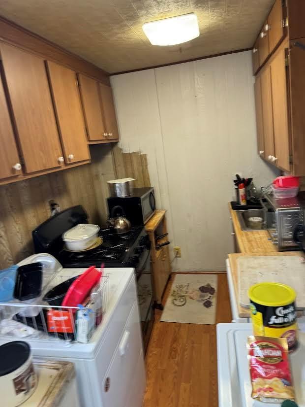kitchen featuring gas range, brown cabinets, light countertops, washer / dryer, and light wood-style floors