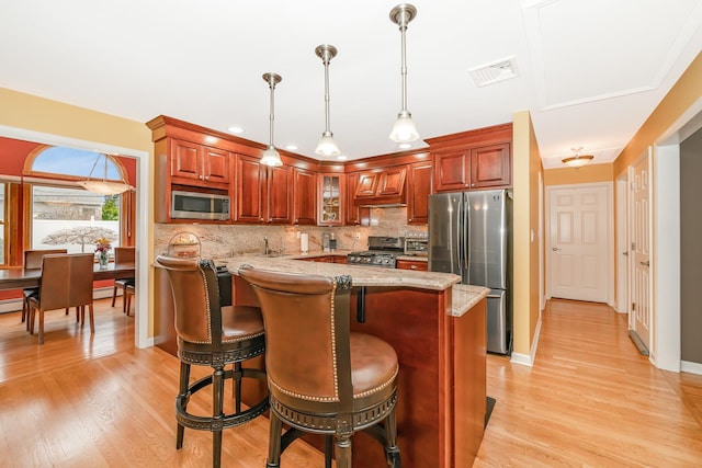 kitchen with light stone counters, light wood-style flooring, stainless steel appliances, backsplash, and visible vents
