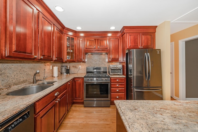 kitchen with a sink, appliances with stainless steel finishes, light stone countertops, and light wood-type flooring
