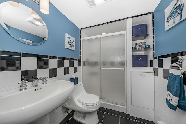 bathroom featuring a sink, tile patterned flooring, toilet, tile walls, and a shower stall