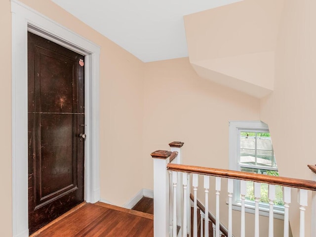 corridor with baseboards, wood finished floors, and an upstairs landing