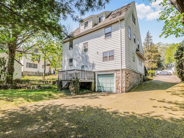 back of house with a garage, a wooden deck, driveway, and stone siding