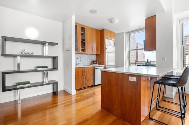 kitchen with a sink, appliances with stainless steel finishes, light wood-style floors, and brown cabinets