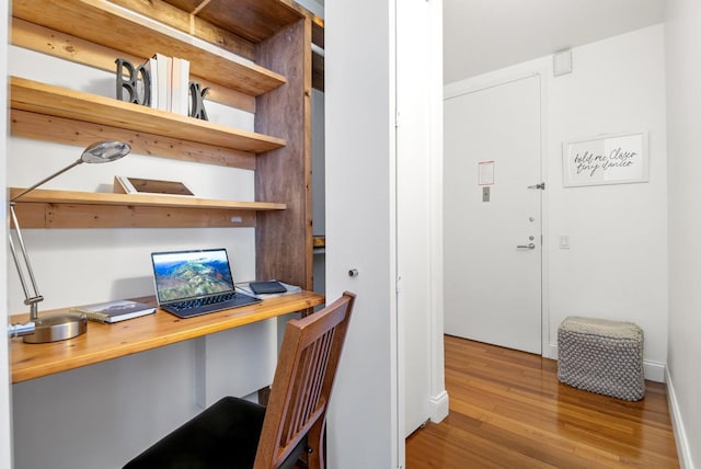 office with baseboards, built in desk, and wood finished floors