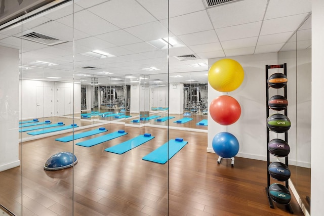 exercise area with baseboards, a drop ceiling, wood finished floors, and visible vents