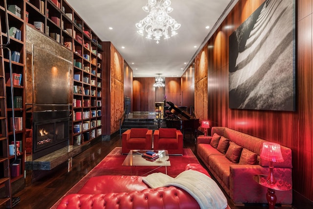 interior space featuring an inviting chandelier, wood-type flooring, wooden walls, a lit fireplace, and built in shelves