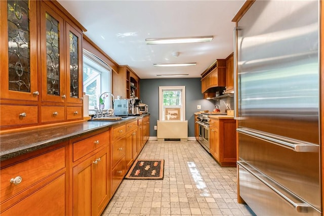 kitchen with high end appliances, glass insert cabinets, baseboards, brown cabinets, and a sink