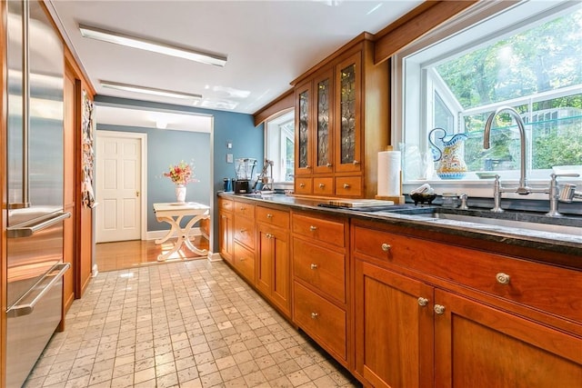 kitchen with brown cabinetry, glass insert cabinets, baseboards, built in refrigerator, and a sink