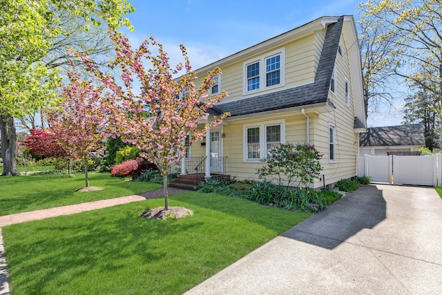 view of front facade with driveway, a front yard, roof with shingles, fence, and a gambrel roof