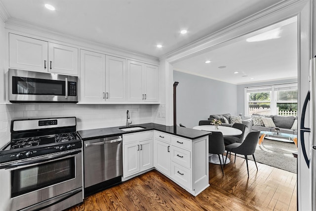 kitchen featuring stainless steel appliances, dark countertops, a sink, and a peninsula