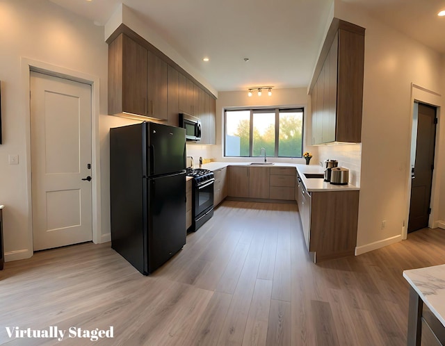 kitchen with a sink, light wood-style flooring, black appliances, and light countertops
