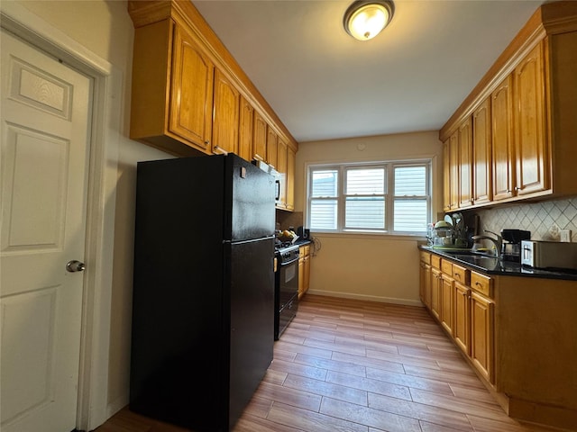 kitchen with decorative backsplash, a sink, baseboards, black appliances, and light wood-style floors