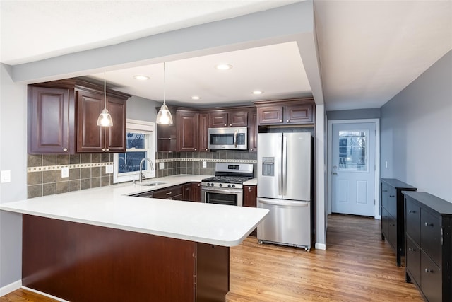 kitchen featuring a peninsula, dark brown cabinetry, light countertops, a sink, and stainless steel appliances