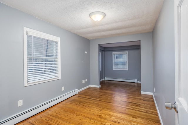 empty room featuring wood finished floors, baseboards, a textured ceiling, and a baseboard heating unit