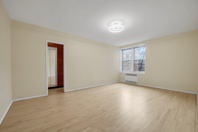 empty room with baseboards, radiator heating unit, and light wood-style floors