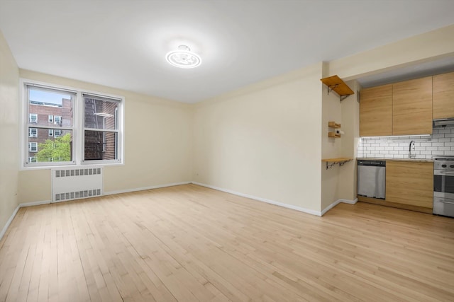 unfurnished living room with radiator heating unit, light wood-style floors, a sink, and baseboards