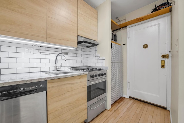 kitchen with tasteful backsplash, under cabinet range hood, appliances with stainless steel finishes, light wood finished floors, and a sink