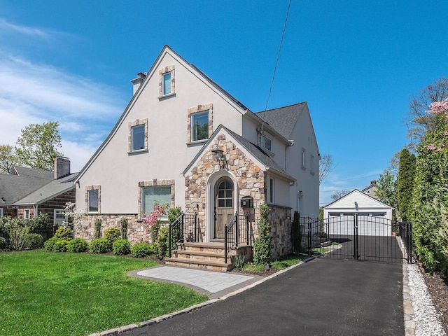 tudor house with stone siding, stucco siding, a gate, a front lawn, and a garage