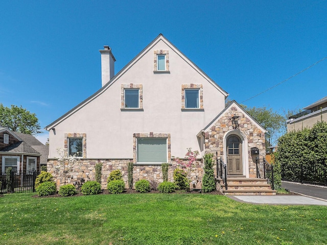 english style home with stucco siding, stone siding, and a chimney