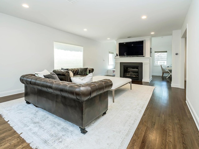 living area featuring a glass covered fireplace, dark wood-type flooring, baseboards, and recessed lighting