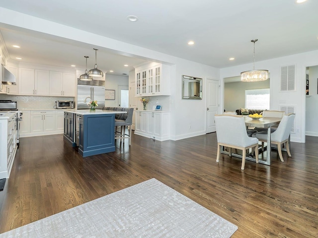 kitchen featuring stainless steel appliances, white cabinetry, a chandelier, a kitchen bar, and dark wood-style flooring