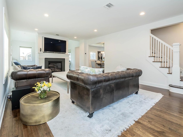 living room with stairway, wood finished floors, healthy amount of natural light, a glass covered fireplace, and recessed lighting