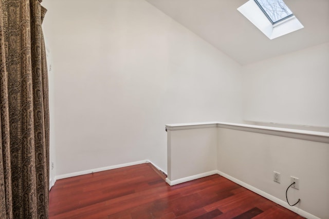 interior space featuring baseboards, vaulted ceiling with skylight, and dark wood-style floors