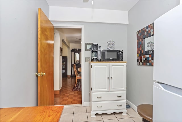 hallway with arched walkways, baseboards, and light tile patterned floors
