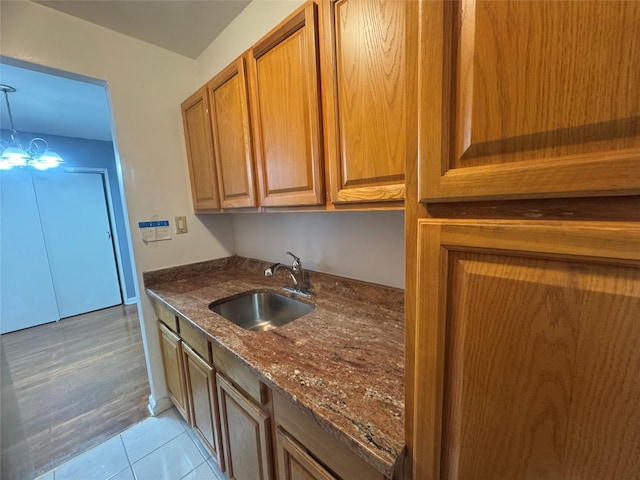 kitchen featuring a sink, dark stone counters, brown cabinets, light tile patterned floors, and hanging light fixtures