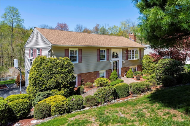 bi-level home featuring brick siding, a chimney, and a shingled roof