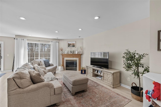 living room featuring a high end fireplace, baseboards, recessed lighting, and light wood-style flooring