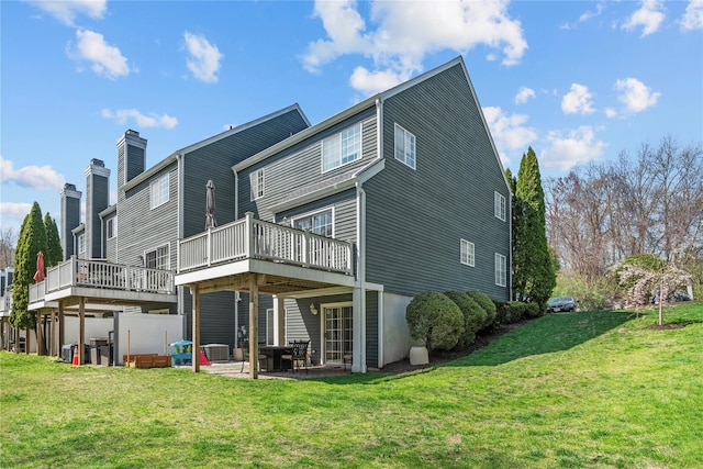 rear view of property featuring a lawn, a chimney, a patio area, and a deck