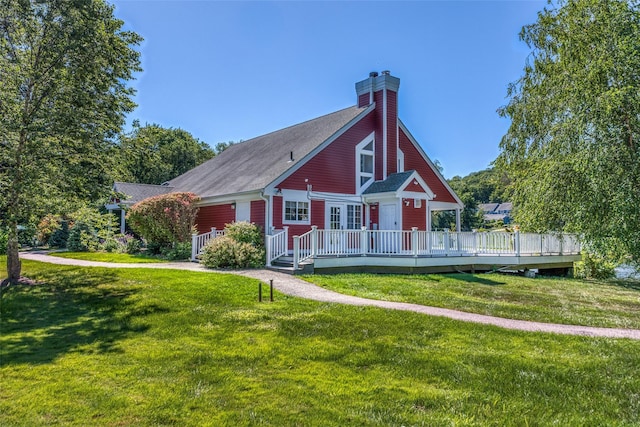 view of front of property with a shingled roof, a wooden deck, a chimney, and a front lawn