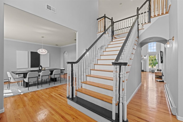 3 Kings Dr, Middletown, NY 10941 - staircase featuring arched walkways, a baseboard heating unit, wood finished floors, a towering ceiling, and baseboards