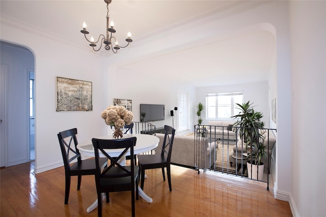 dining space with an inviting chandelier, wood finished floors, baseboards, and arched walkways