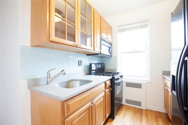 kitchen with radiator, a sink, light wood-style floors, stainless steel fridge, and black gas range oven