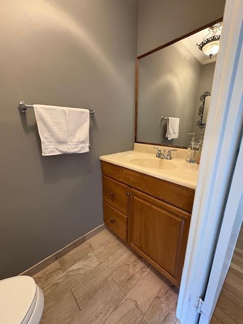 half bath featuring crown molding, toilet, and vanity