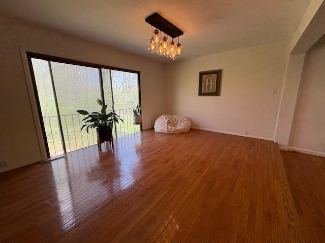 spare room with a chandelier, hardwood / wood-style floors, and baseboards